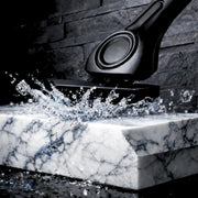 Black metal shaving razor on a marble surface with water splashing around it